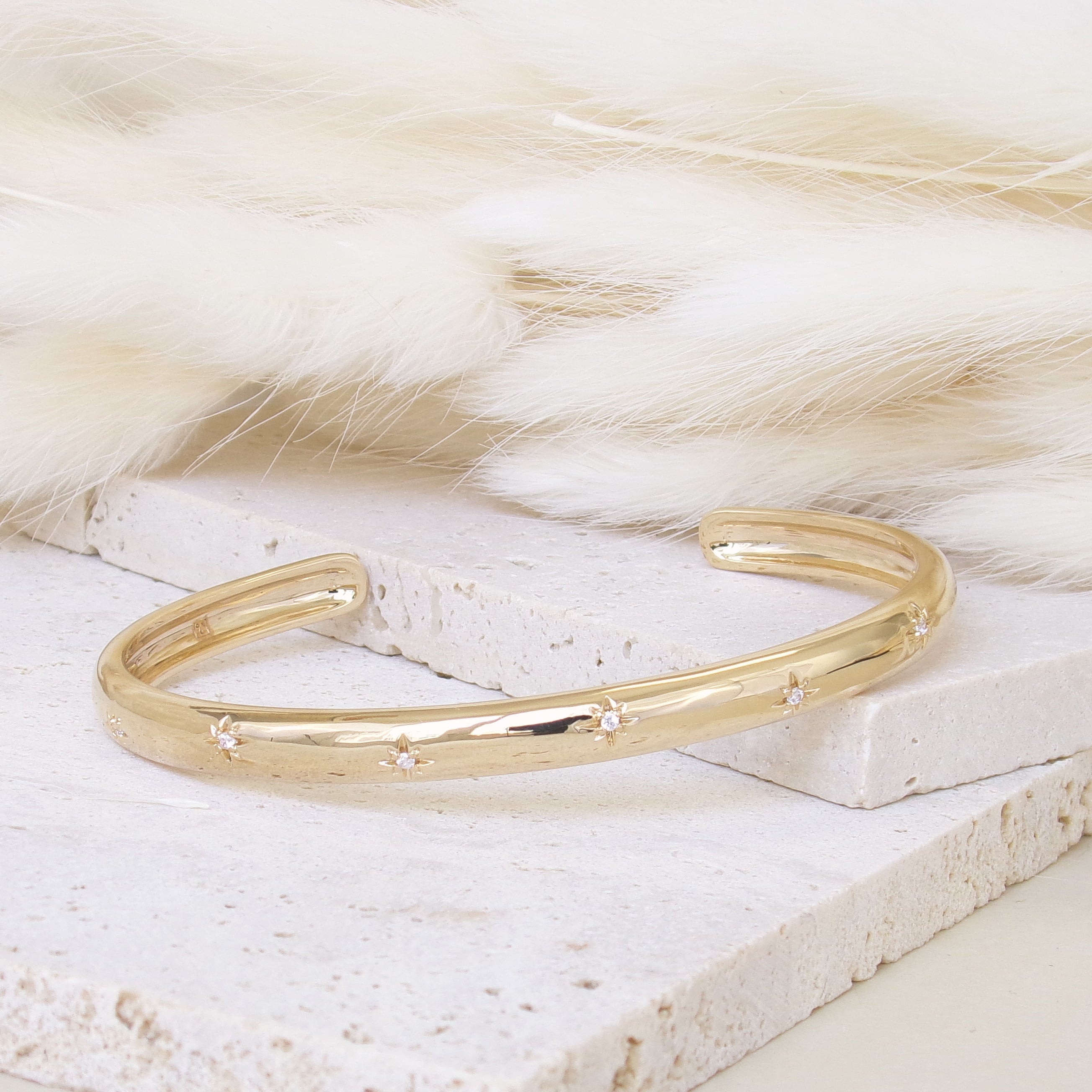 Bracelet jonc ouvert Aria en plaqué or 18 carats – Plongez dans un univers magique avec ce bijou raffiné, orné de deux étoiles serties d’oxydes de zirconium scintillants. Son design élégant sublime votre style et apporte une touche lumineuse à toutes vos tenues. Diamètre : 58 mm. Conçu en laiton avec un placage 3 microns et poinçon garantissant qualité et durabilité.