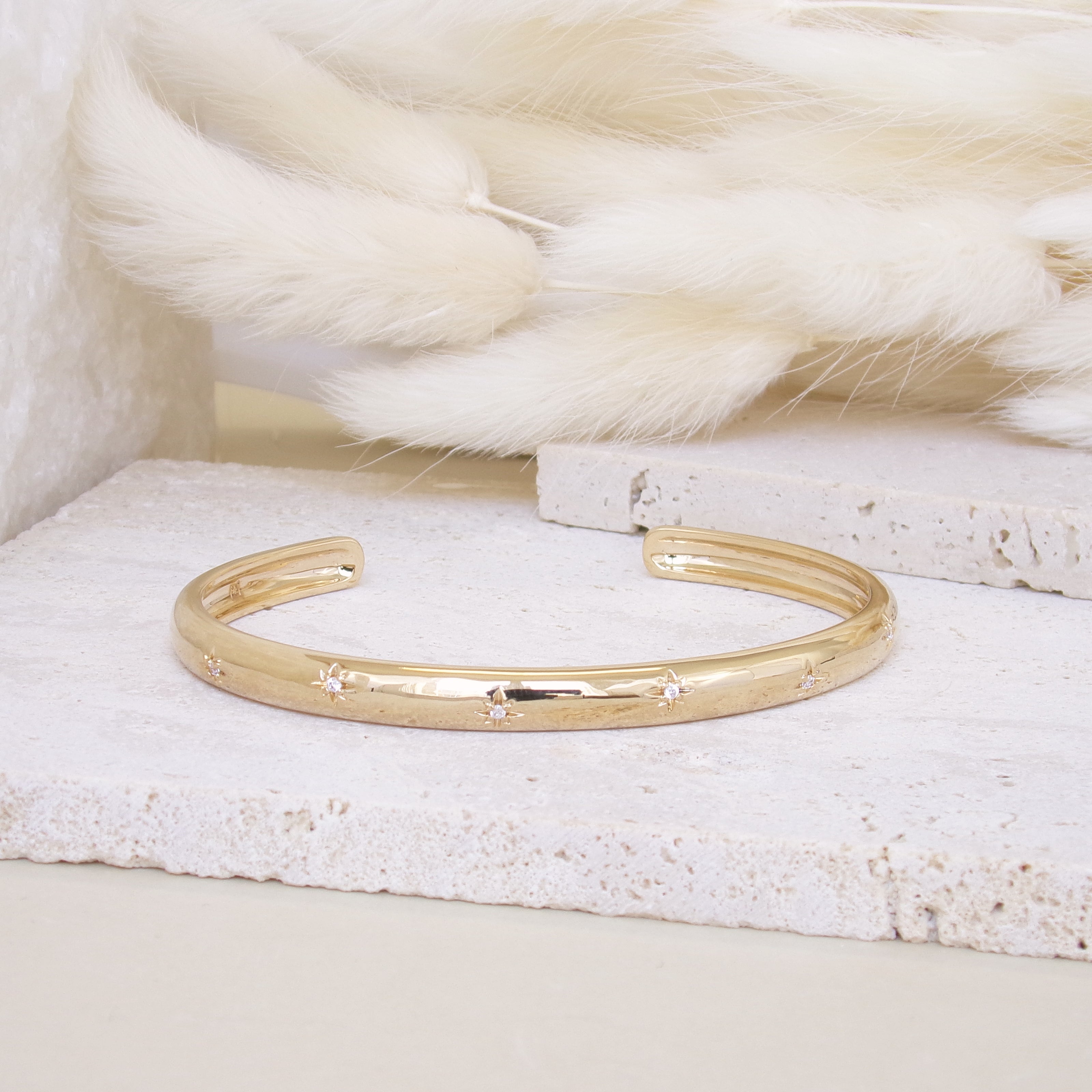 Bracelet jonc ouvert Aria en plaqué or 18 carats – Plongez dans un univers magique avec ce bijou raffiné, orné de deux étoiles serties d’oxydes de zirconium scintillants. Son design élégant sublime votre style et apporte une touche lumineuse à toutes vos tenues. Diamètre : 58 mm. Conçu en laiton avec un placage 3 microns et poinçon garantissant qualité et durabilité.