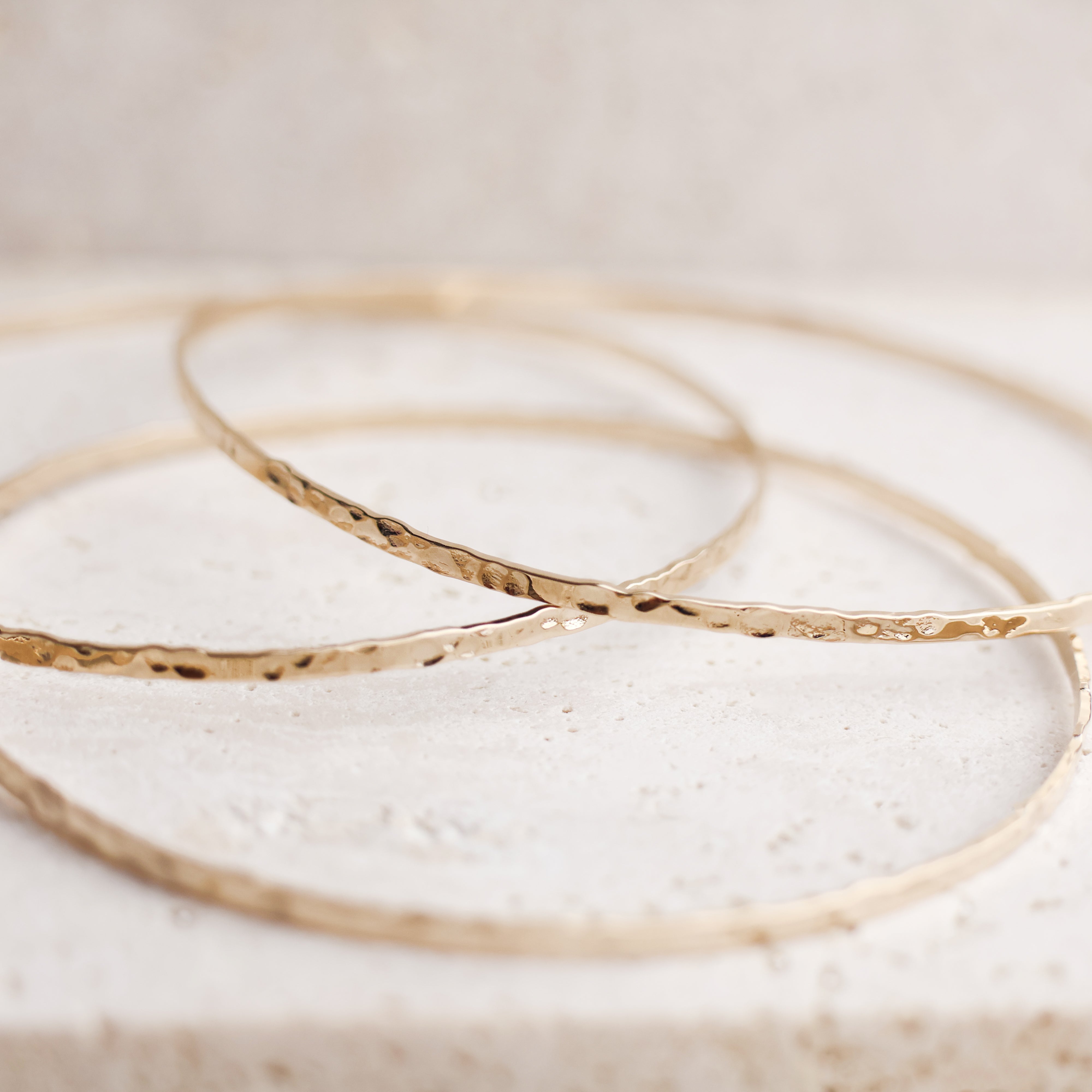 Bracelet Rosie en plaqué or 18 carats – Jonc élégant avec une finition martelée à l'extérieur et un intérieur lisse, offrant un jeu subtil de textures. Son éclat raffiné apporte une touche lumineuse à vos tenues et sublime votre style avec finesse. Diamètre 62 mm, conçu en laiton avec un placage 3 microns et poinçon garantissant qualité et durabilité.