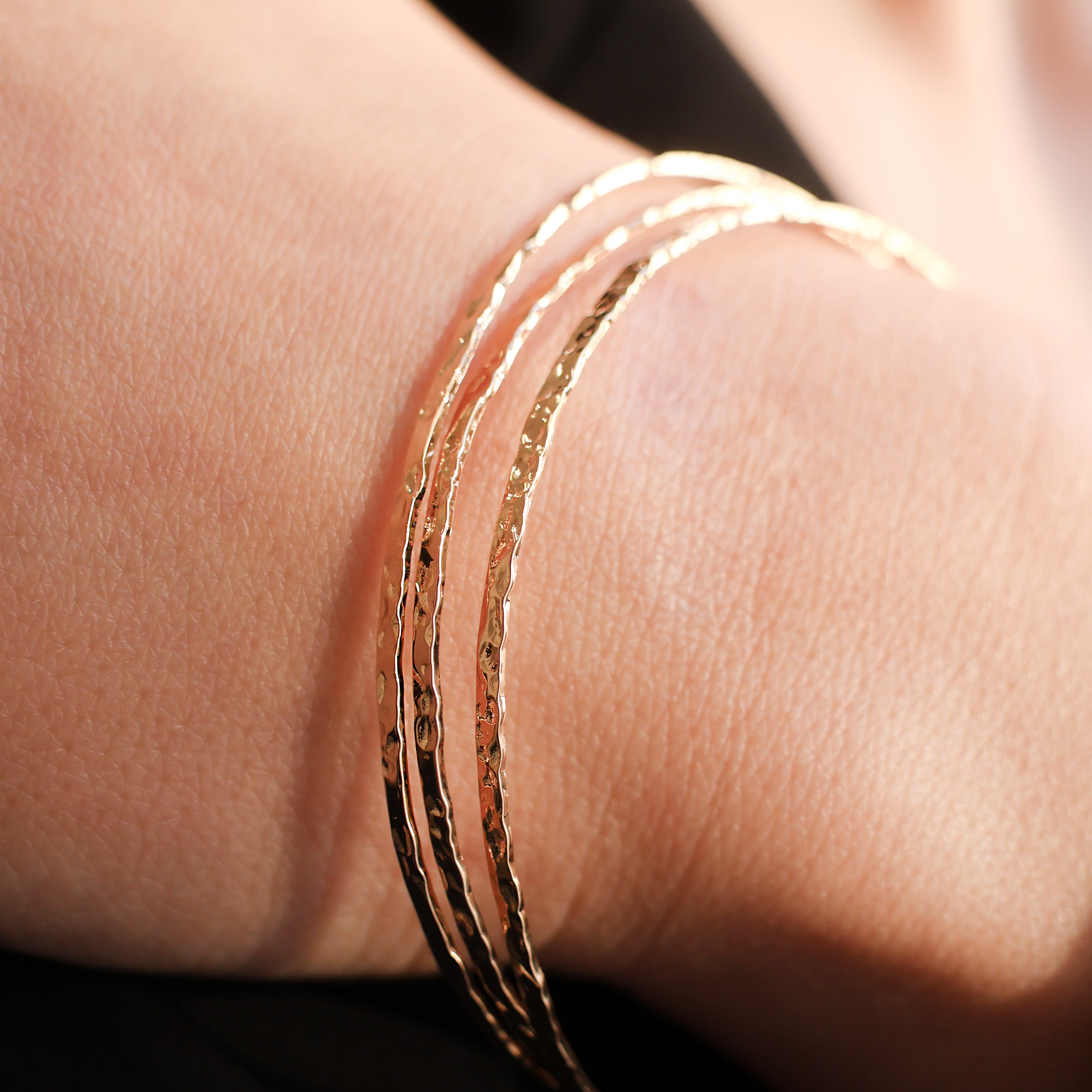 Bracelet Rosie en plaqué or 18 carats – Jonc élégant avec une finition martelée à l'extérieur et un intérieur lisse, offrant un jeu subtil de textures. Son éclat raffiné apporte une touche lumineuse à vos tenues et sublime votre style avec finesse. Diamètre 62 mm, conçu en laiton avec un placage 3 microns et poinçon garantissant qualité et durabilité.