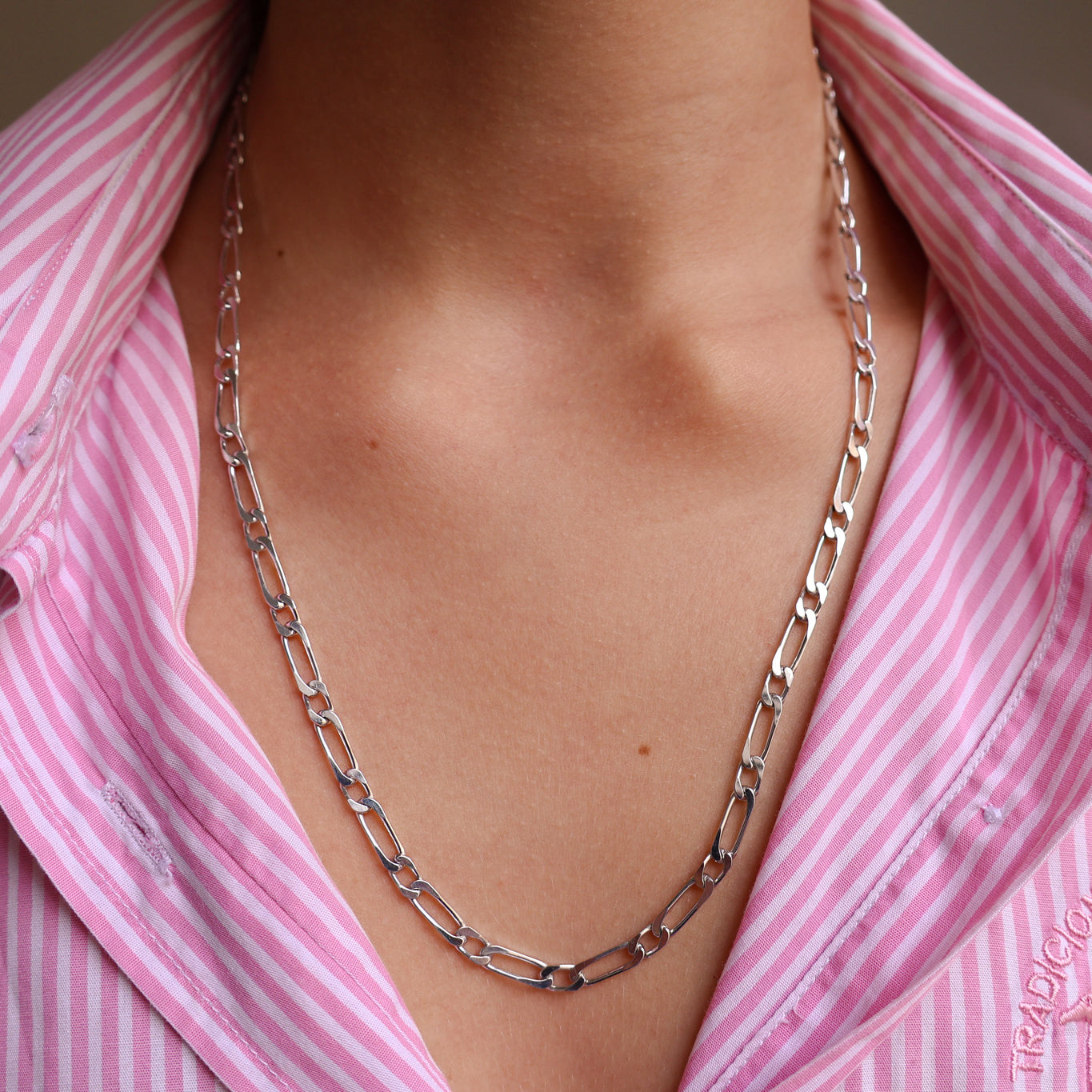 Chaîne en argent 925 rhodié portée sur un col de chemise rayé rose, bijou unisexe à mailles plates, indémodable et minimaliste.
